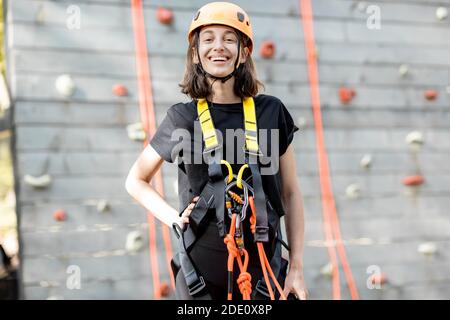 Portrait d'une jeune femme bien équipée debout devant du mur d'escalade au parc d'attractions Banque D'Images