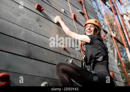 Jeune femme bien équipée grimpant le mur à l'extérieur dans le parc pour le divertissement sportif Banque D'Images