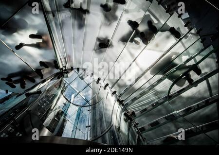 Les gens qui marchent en haut et en bas d'un escalier en verre vu d'en bas apparaissent comme des silhouettes contre la lumière. Aucune face Banque D'Images