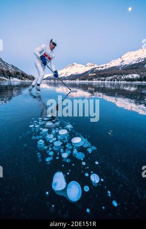 Joueur de hockey sur glace homme patinant sur le lac Sils couvert de bulles de glace au crépuscule, Engadine, canton de Graubunden, Suisse, Europe Banque D'Images