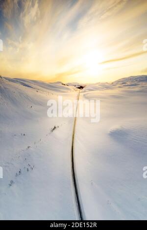 Vue aérienne du ciel brûlant à l'aube sur la route pittoresque traversant les montagnes enneigées, Sennalandet, Alta, Troms og Finnmark, Arctic, Norvège Banque D'Images