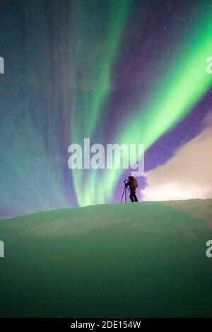 Homme avec trépied photographiant les aurores boréales (Aurora Borealis) debout dans la neige, Skarsvag, Nordkapp, Troms og Finnmark, Norvège Banque D'Images