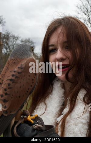 Une jeune femme aux longs cheveux bruns, souriant et tenant un petit Kestrel commun brun (falco tinnunculus) Banque D'Images