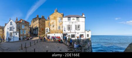 Vue sur le White Washed Bay Hotel et les visiteurs au port de Robin Hood Bay, North Yorkshire, Angleterre, Royaume-Uni, Europe Banque D'Images