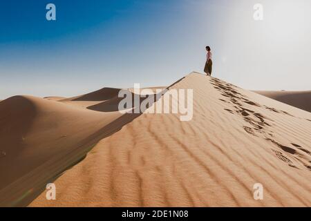 Femme au milieu du désert, marche au bord de la dune, scène de tranquillité, empreintes de pas dans le sable, ciel bleu Banque D'Images