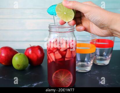 Main de l'homme en pressant une tranche de citron vert dans la bouteille De la Sangria du vin rouge Banque D'Images