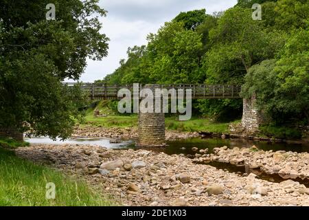 Passerelle au-dessus de la rivière Swale dans une campagne pittoresque (eau peu profonde par temps sec en été, rochers de lit de rivière) - rampes Holme Bridge, Yorkshire Dales, Royaume-Uni. Banque D'Images