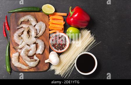 Cuisine asiatique. Ingrédients pour la cuisson de nouilles sautées avec crevettes sur une table sombre, vue du dessus Banque D'Images