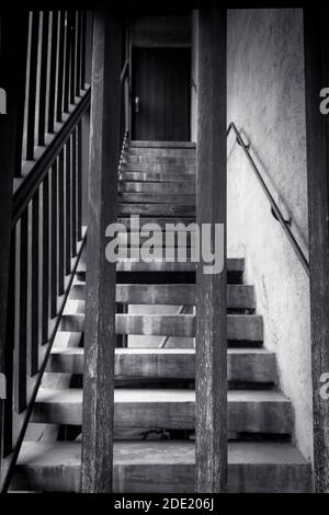 Gros plan image en noir et blanc d'escaliers en bois menant vers le haut à une porte verrouillée, vue par une porte barrée, Banque D'Images