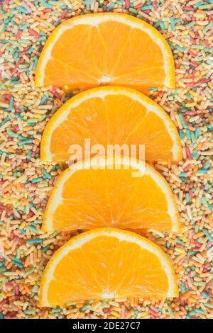 Tranches d'orange coupées en deux sur une base de nouilles colorées amusantes. Desserts faits maison et sucettes de sucre. Banque D'Images