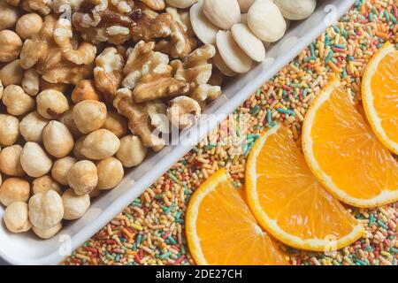 Un assortiment de fruits secs, de noix, d'amandes et de noisettes mélangés avec des tranches d'orange sur des nouilles de sucre colorées. Desserts de cuisine créatifs Banque D'Images