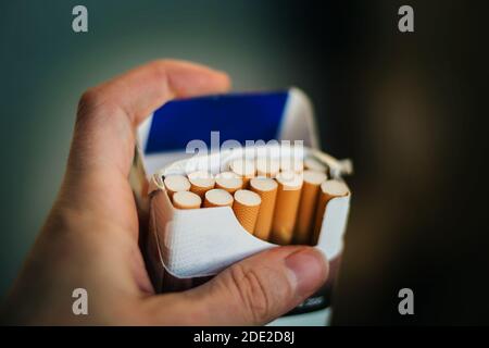 Un homme tient un paquet ouvert de cigarettes avec des filtres orange dans sa main. Le mal de fumer. Banque D'Images