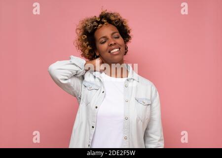 Jeune femme afro-américaine souffrant de douleurs au cou. Studio tourné sur un mur rose. Banque D'Images