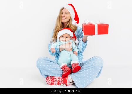 Une jeune mère, le jour de Noël donne un cadeau à un nouveau-né, une fille tient un bébé dans ses bras avec un cadeau de Noël, le matin de Noël dans la famille Banque D'Images