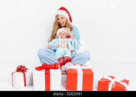 Une jeune mère, le jour de Noël donne un cadeau à un nouveau-né, une fille tient un bébé dans ses bras avec un cadeau de Noël, le matin de Noël dans la famille Banque D'Images