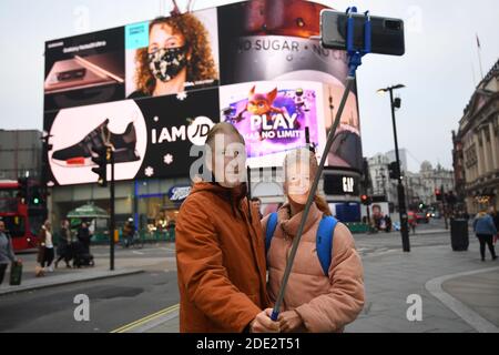 Deux personnes prennent un selfie portant des masques du Prince de Galles et de la reine Elizabeth II devant les écrans de Piccadilly Circus, Londres, dans la dernière semaine d'un confinement national de quatre semaines pour freiner la propagation du coronavirus. Banque D'Images