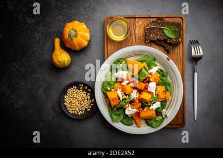 Salade avec citrouille rôtie, fromage, épinards, pignons de pin et assaisonnements sur fond sombre, vue du dessus Banque D'Images