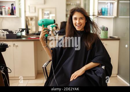 Une cliente heureuse utilisant un sèche-cheveux, un salon de coiffure Banque D'Images