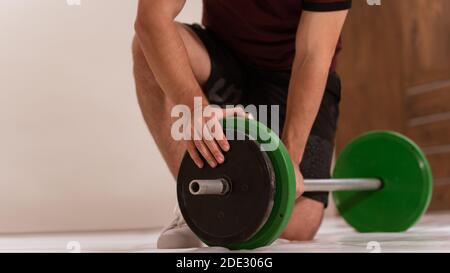 Un jeune homme s'incline sur un genou en préparant des accessoires de fitness noir et vert, de l'équipement pour le concept d'entraînement de poids. Équipement de sport pour hommes pour l'entraînement Banque D'Images