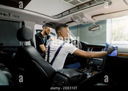 Service de voiture et station de détail. Vue arrière en intérieur de deux travailleurs multiethniques professionnels, offrant un nettoyage et un essuyage de l'intérieur du véhicule Banque D'Images