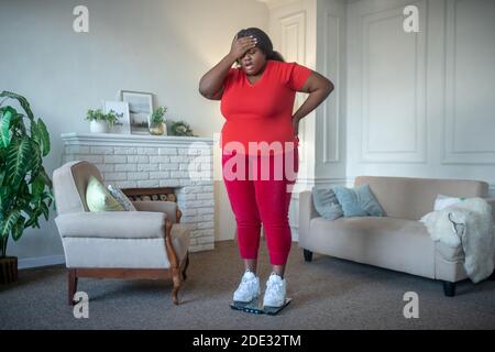 Femme afro-américaine de taille plus vérifiant son poids et regardant frustré Banque D'Images
