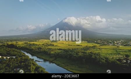 Rivière à flanc de coteau au volcan en éruption avec pelouse verte à l'antenne de campagne des Philippines. Champs, vallée, prés de personne nature paysage. Le paysage cinématographique du mont Mayon éclate à la brume Banque D'Images