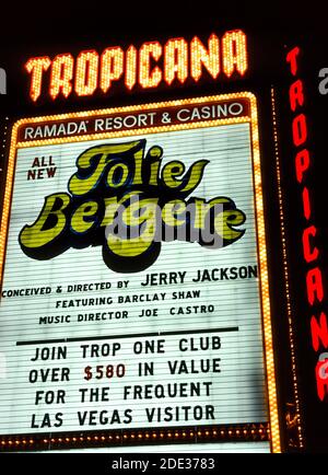Les néons et autres lumières ont fait ressortir cette enseigne extérieure pour le Tropicana Resort & Casino la nuit le long de Las Vegas Boulevard, mieux connu sous le nom de Strip, une route bordée d'hôtels et de casinos spectaculaires, juste au sud des limites de la ville de Las Vegas, Nevada, États-Unis. Le Tropicana a ouvert ses portes en 1957 et est depuis présent dans cette célèbre destination désertique bien connue pour ses jeux et ses bons moments. Cette photographie historique a été prise en 1983 lorsque le Tropicana appartenait à la chaîne d'hôtels Ramada. Le panneau annonce les divertissements de l'hôtel, le spectacle Folies Bergére.