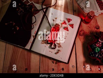 Image d'une bouteille avec du liquide rouge et 4 dés d4 sur un tomon en cuir. Jeux de cartes et un sac de dés plein avec différents types de dés sur un woo Banque D'Images