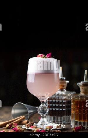 Cocktail femelle rose avec mousse dans un verre. Décoré de rose séchée. En arrière-plan est visible barman inventaire Banque D'Images