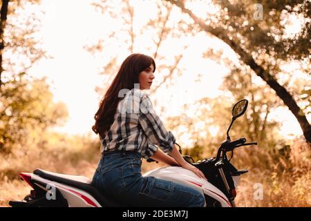 Portrait d'une jeune femme assise sur une moto au milieu d'arbres Banque D'Images