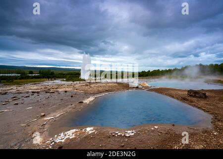 Vue panoramique de l'étang bleu sur la zone géothermique avec geyser Strokkur en arrière-plan, Geysir, Islande Banque D'Images