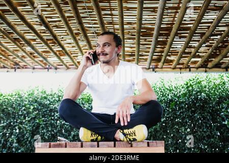 Homme mexicain utilisant un smartphone assis à pieds croisés, concept de travail à domicile et de style de vie en Amérique latine Banque D'Images