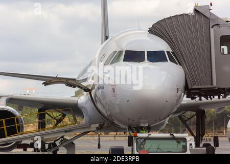 Vue avant de l'avion passager de type Airbus A320 avec courroie transporteuse de bagages à travers la porte de chargement et passerelle d'embarquement des passagers connectée. Banque D'Images