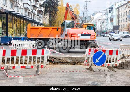 Une lourde machinerie de route, une pelle hydraulique et un camion sur une section clôturée d'un trottoir de rue de ville sont impliqués dans la réparation d'une conduite de chauffage principale. Banque D'Images