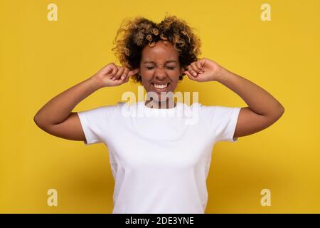 Jeune femme africaine aux oreilles bouchées de cheveux bouclés. Studio tourné sur un mur jaune. Banque D'Images