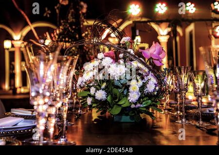 Table en bois montée avec des plaques et de belles lunettes pour une illusion, ornée de fleurs et de lumières dans une Hacienda la nuit Banque D'Images