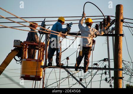 Trois hommes de ligne électriques travaillant en hauteur sur les câbles de rue, l'un sur le dessus de la grue et l'autre sur le dessus d'un poteau fixé par des ceintures Banque D'Images