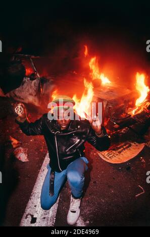 Manifestation contre la guerre du Golfe le 17 janvier 1991. San Francisco, Californie, États-Unis. Un jeune homme noir portant un chapeau de couleur panafricaine et portant un signe de paix se met à genoux devant une voiture de police en feu à l'entrée du pont de la baie de San Francisco. Le jeune homme photographié tentait d'arrêter la violence pendant la manifestation. REMARQUE : il s'agit d'une photo de fichier prise en 1991. Banque D'Images