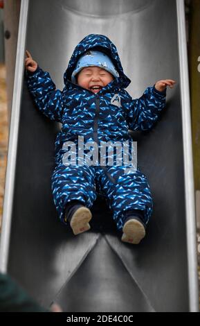 Tout-petit, garçon, 15 mois, multiethnique, sur le toboggan pour enfants, rire, Stuttgart, Bade-Wurtemberg, Allemagne Banque D'Images