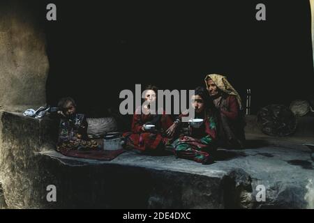 Une vieille femme, deux filles et un bébé dans le fumoir d'une maison de boue traditionnelle, les filles buvant du thé au lait, Sarad-e-Broghil, couloir de Wakhan Banque D'Images