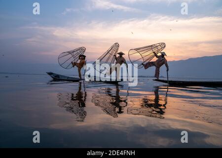 Trois pêcheurs traditionnels posent debout sur leurs petits bateaux, au lever du soleil, au lac Inle, au Myanmar Banque D'Images