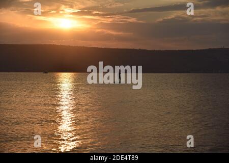 Un homme navigue sur un panneau SUP dans un grand lac au lever du soleil. Stand up paddle board - des loisirs actifs dans la nature. La mer de Galilée, le lac Tibériade, Kinneret, Kinnereth. Photo de haute qualité. Banque D'Images