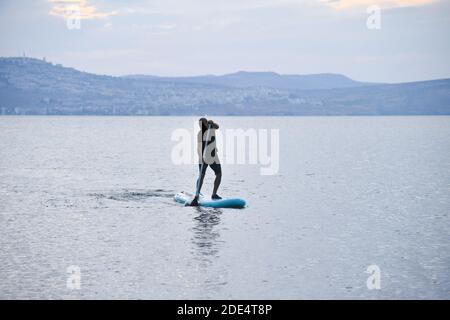 Un homme navigue sur un panneau SUP dans un grand lac au lever du soleil. Stand up paddle board - des loisirs actifs dans la nature. La mer de Galilée, le lac Tibériade, Kinneret, Kinnereth. Photo de haute qualité. Banque D'Images