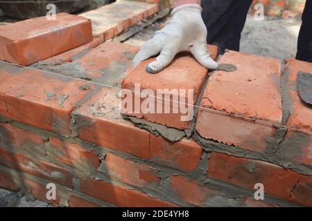 Briques mains dans des gants de maçonnerie briqueter nouveau mur de maison. Banque D'Images