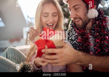 beardy guy donnant un cadeau à sa petite amie pour noël, avec chapeau de père noël sur sa tête, souriant. concept christmastime Banque D'Images