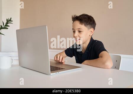 Un garçon d'école assis sur un bureau avec un ordinateur portable écrit des leçons d'école pendant les devoirs. Banque D'Images