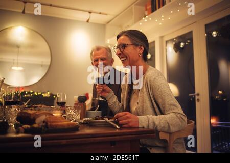 Couple senior appréciant un dîner de noël en famille. Femme mature tenant un verre de vin parlant et souriant à la table du dîner. Banque D'Images