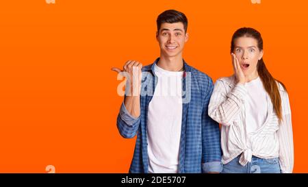 Jeune belle femme avec la bouche ouverte regarder la caméra et l'homme choqué, montre le doigt à l'espace libre Banque D'Images