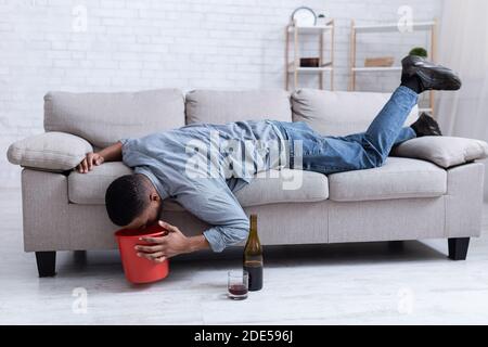 Homme ivre vomissant dans le seau après avoir bu du vin couché à l'intérieur Banque D'Images