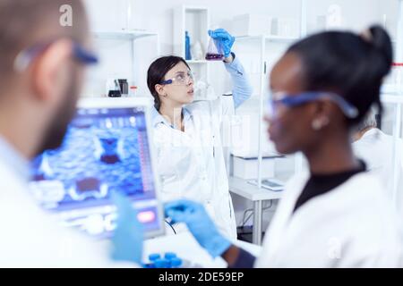 Test de chimie examinant un échantillon scientifique dans un laboratoire très occupé. Une équipe multiethnique de chercheurs médicaux travaillant ensemble dans un laboratoire stérile portant des lunettes et des gants de protection. Banque D'Images